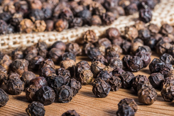 Black pepper grains on a wooden background and burlap.