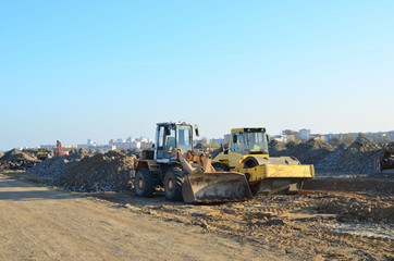 Soil Compactor and  wheel loader at construction site. Vibration single-cylinder road roller leveling the ground for the construct of the foundation for residential building, office, shopping center.
