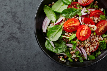 Buckwheat salad with cherry tomatoes, spinach, spring onion and mint leaves. Copy space. Dark stone background