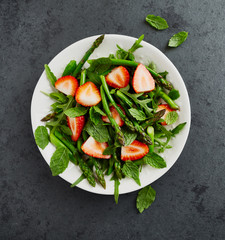 Green asparagus, arugula and strawberry salad with mint leaves. From above