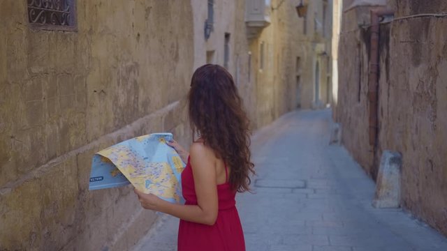 A young woman tourist is standing in the old city, with a map in his hands and looking for his whereabouts. Tourist with a map.