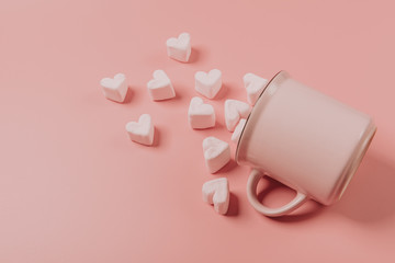 a pink mug lies on its side against a pink background, light-pink marshmallows sprinkled from it in the form of hearts