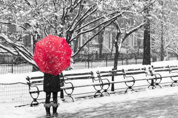 Woman with red umbrella walking through a snowy black and white winter scene in New York City