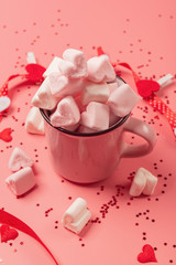 pink mug on a pink background filled with marshmallows in the form of hearts. valentine's day holiday concept