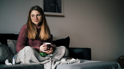 traurige junge Frau ist krank und sitz auf Sofa und trinkt Tee