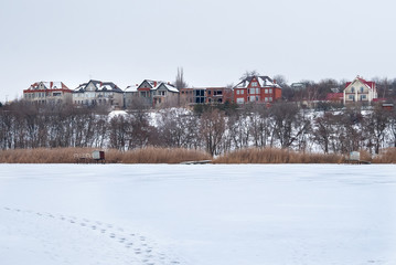 Fototapeta premium Traces on the frozen river. Houses can be seen on the other side of the hill