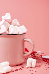 pink mug on a pink background filled with marshmallows in the form of hearts. valentine's day holiday concept