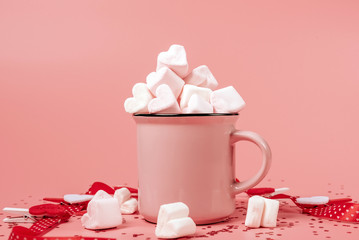 pink mug on a pink background filled with marshmallows in the form of hearts. valentine's day...