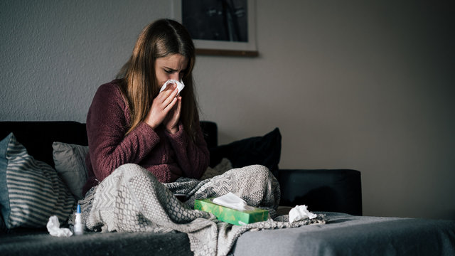junge Frau ist erkältet und sitz auf Sofa und putzt sich die Nase