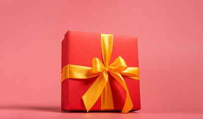 red box tied with a gold ribbon. the ribbon is tied on a box in the form of a beautiful bow. holiday gift concept