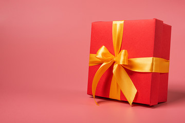 red box tied with a gold ribbon. the ribbon is tied on a box in the form of a beautiful bow. holiday gift concept
