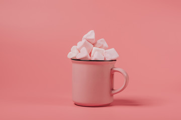 pink mug on a pink background filled with marshmallows in the form of hearts. valentine's day holiday concept