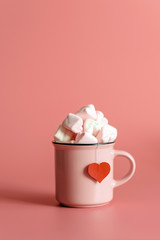 pink mug on a pink background filled with marshmallows in the form of hearts. valentine's day holiday concept