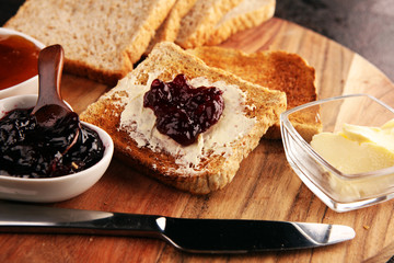 Toast bread with homemade strawberry jam and apricot marmalade on rustic table served with butter...