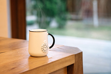 A soaring white cup with a picture of a pocket watch on a wooden table.