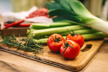 Three ripe tasty tomatoes on a wooden board on a background of green vegetables. Food.