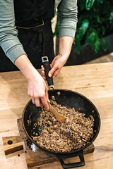 Professional chef hands prepare meat filling for a pie in a pan while stirring with a wooden spatula.