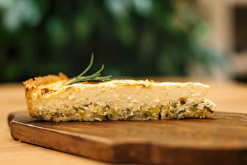 appetizing piece of quiche pie with creamy filling and leek on a wooden cutaway sectional view.