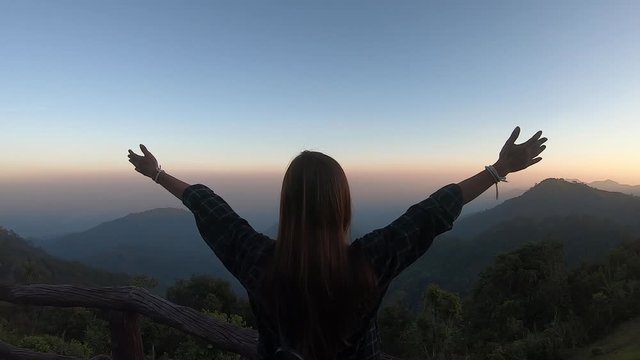 Back view of a happy Woman standing with arms raised up during beautiful sunrise at morning, Enjoy nature At the viewpoint of Chiang Mai, Thailand
