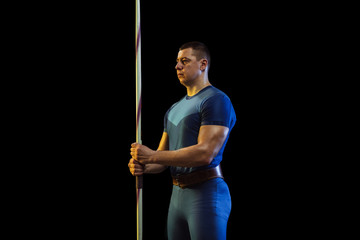 Male athlete practicing in throwing javelin on black background in neon light. Professional sportsman posing confident. Concept of healthy lifestyle, movement, activity, competition. Copyspace.