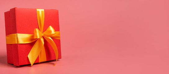 red box tied with a gold ribbon. the ribbon is tied on a box in the form of a beautiful bow. holiday gift concept
