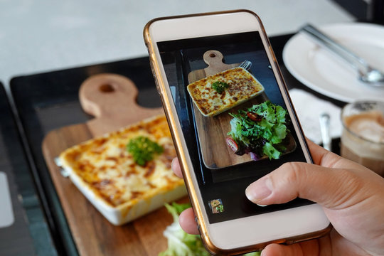 Selective focus smartphone picture which Woman hands takes photography by smartphone of food  lasagne with pork tomatoes, cheese sauce ,social media concept