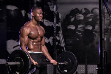Fototapeta na wymiar Muscular African American shirtless, sweaty male bodybuilding athlete does barbell curls in a dark grungy gym with dramatic lighting flare 
