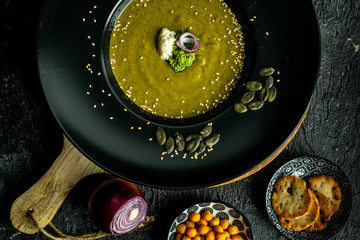 broccoli soup with the addition of pumpkin seeds, sesame on a black plate, next to crispy, soy-nut additions
