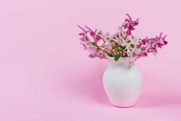 bouquet of small forest pink, white and purple red flowers in a white vase on a pink background with copy space