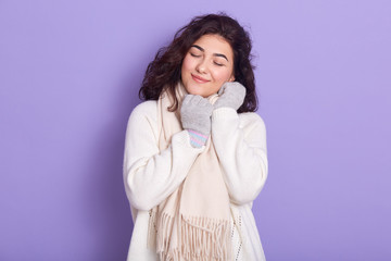 Pleasant positive beautiful female closing eyes, smiling sincerely, spending time alone, wearing...
