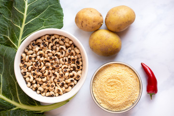 Overhead view of Uncooked blackeye Peas, Collard Greens, cornmeal, potatoes and red pepper in preparation for cooking