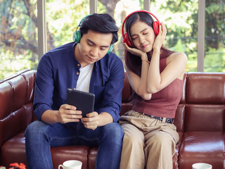 Fototapeta premium young Asian couple sitting in living room at home listen to the music from tablet , a man pick a song while woman close her eyes and listen to music happily.