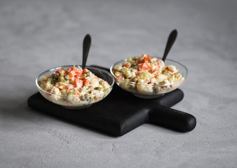 Russian salad with chicken, potatoes, eggs, carrots, green peas and cucumber, appetizer on a light gray background
