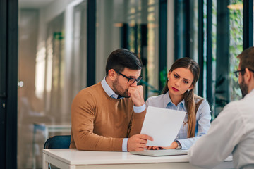 Worried couple looking at paper document in the office of financial adviser.