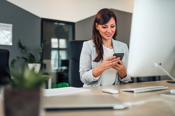 Businesswoman using smart phone in modern office, portrait.