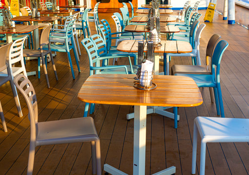 Wooden deck chairs and tables on the outdoor deck of a cruise ship