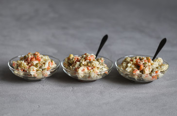 Russian salad with chicken, potatoes, eggs, carrots, green peas and cucumber, appetizer on a light gray background