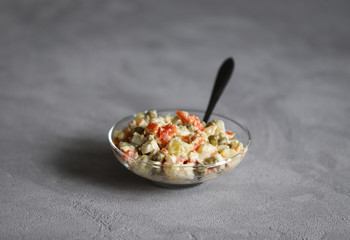 Russian salad with chicken, potatoes, eggs, carrots, green peas and cucumber, appetizer on a light gray background