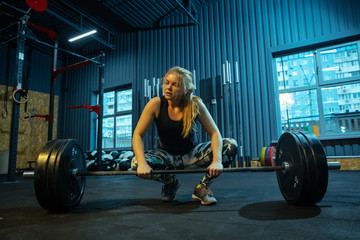 Fototapeta na wymiar Caucasian teenage girl practicing in weightlifting in gym. Female sportive model training with barbell, looks concentrated and confident. Body building, healthy lifestyle, movement and action concept.