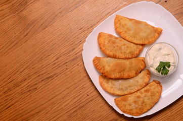 Uzbek eastern Tatar cuisine, cheburek with meat and suluguni cheese in a white plate with vegetables and greens on a wooden table.
