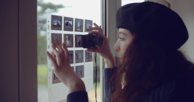 young woman looks at photographic slides near the window