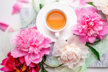 Peonies and cup of tea on white background. Spring flowers. Spring breakfast background. Greeting card for Valentine's Woman's Mother's Day, wedding.