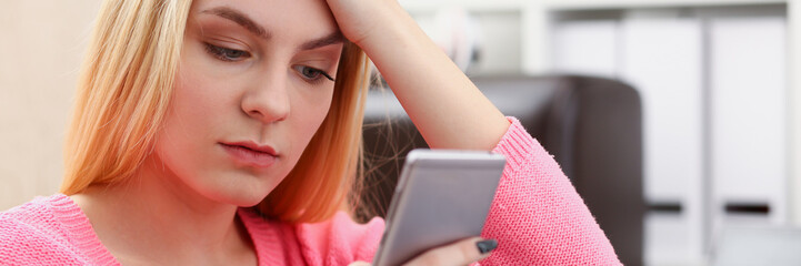 Obraz premium young pretty blond womansit on sofa hold smartphone in hands