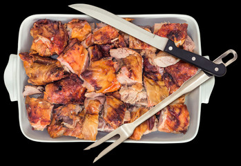 Plateful of Fresh Spit Roasted Pork Thigh Meat Slices Offered in White Ceramic Casserole Pan with Serving Knife and Fork Isolated on Black Background