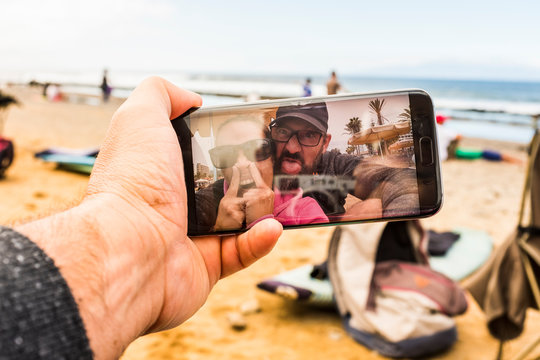 Couple of adult crazy man and woman in video call at the beach doing funny expression - happy people with technology phone device making crazy - joy and nice adults at the beach during vacation