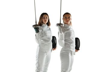 Teen girls in fencing costumes with swords in hands isolated on white studio background. Young...