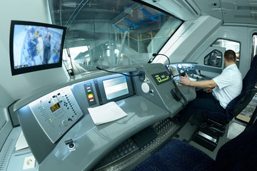 At the cabin of the passenger train. Train driver sitting of locomotive in front of the dashboard and putting hand on the start lever