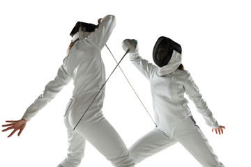 Teen girls in fencing costumes with swords in hands isolated on white studio background. Young...