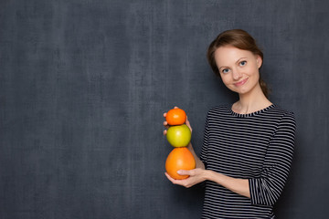 Portrait of happy woman smiling and holding colorful stack of fruits