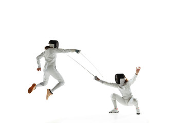 Teen girls in fencing costumes with swords in hands isolated on white studio background. Young female models practicing and training in motion, action. Copyspace. Sport, youth, healthy lifestyle.